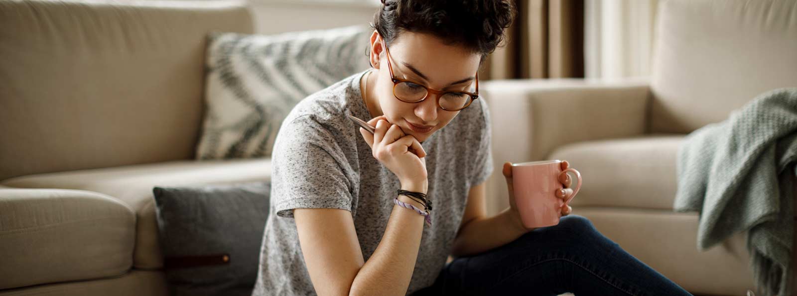 Woman sitting and reviewing something in her home while holding a coffee mug