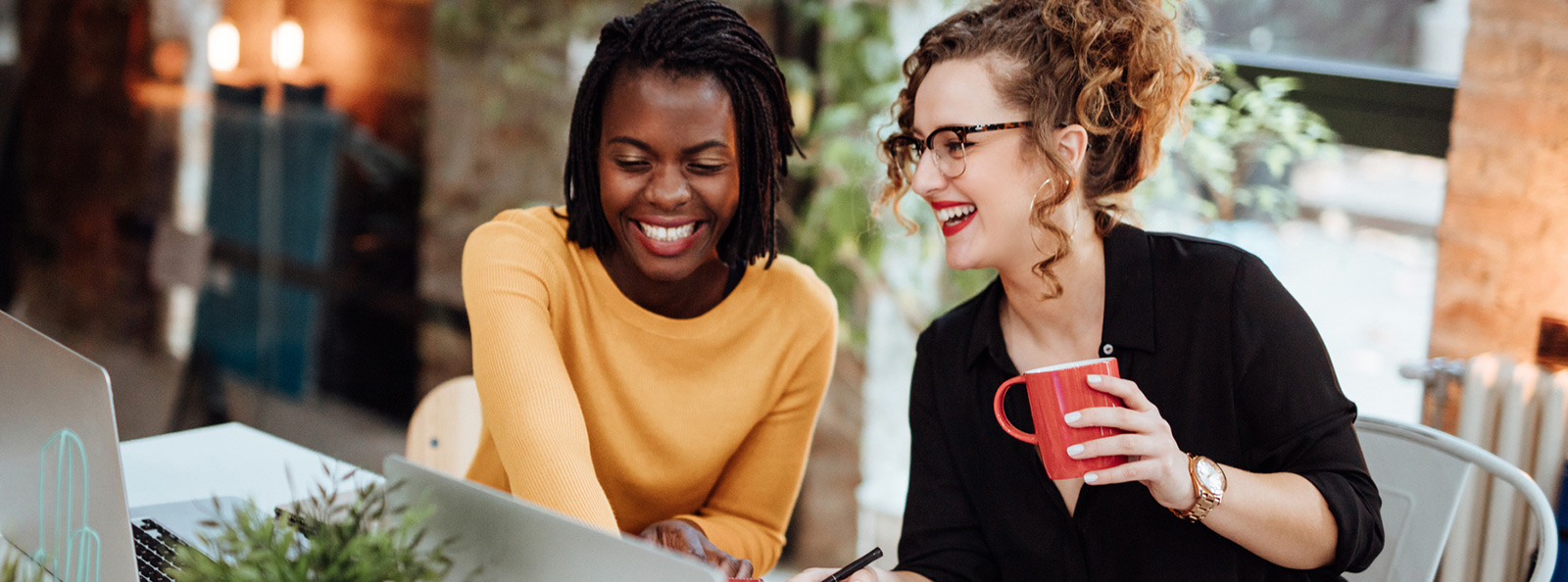 Women smiling outside while looking at their laptops